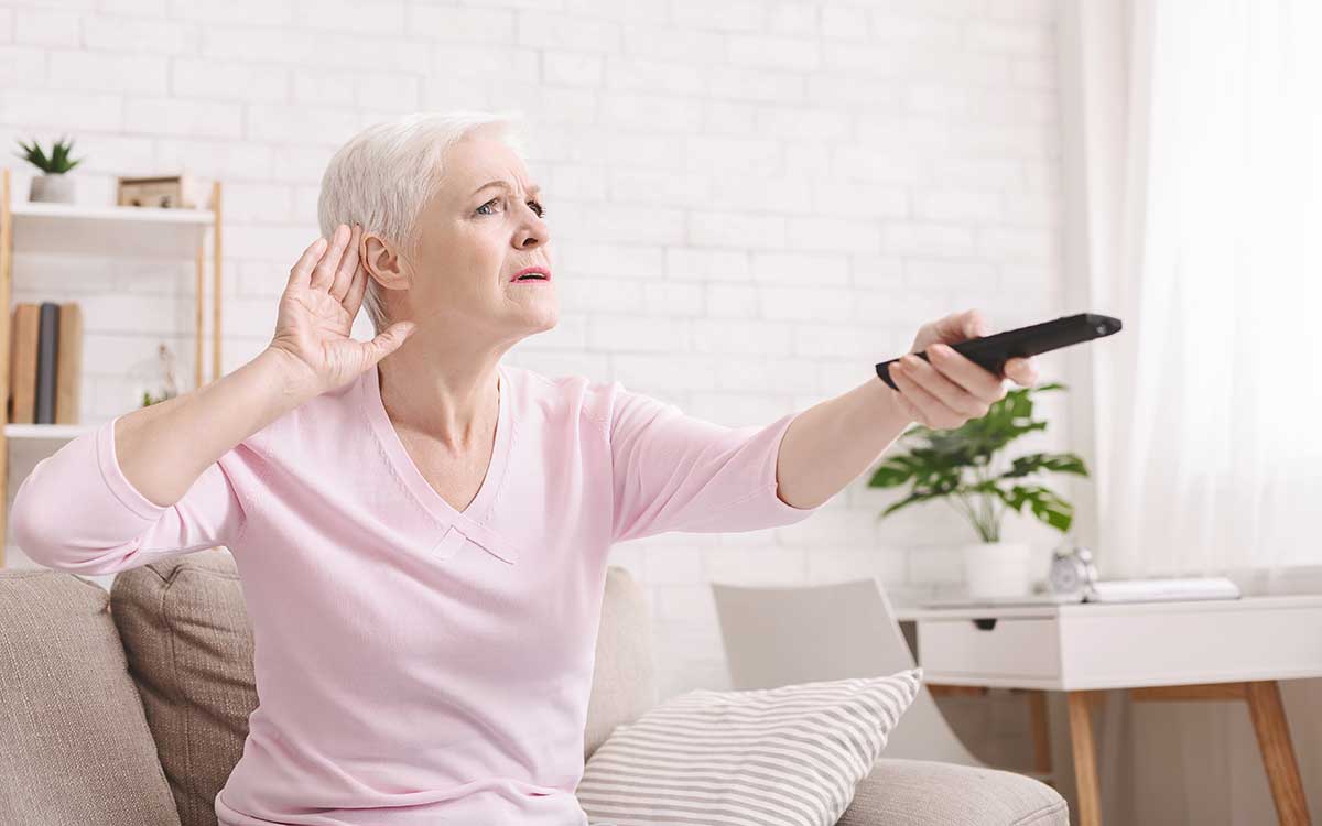 elderly woman with a remote holding her ear with a hand