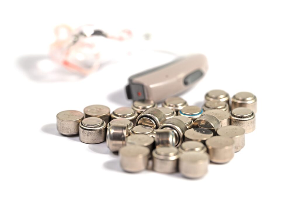 Pile of disposable hearing aid batteries in front of a behind-the-ear hearing aid, for battery life tips from Professional Hearing Center in Fremont, NE